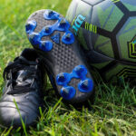 pair of blue soccer cleats that look like they are fit for a toddler sitting on the grass